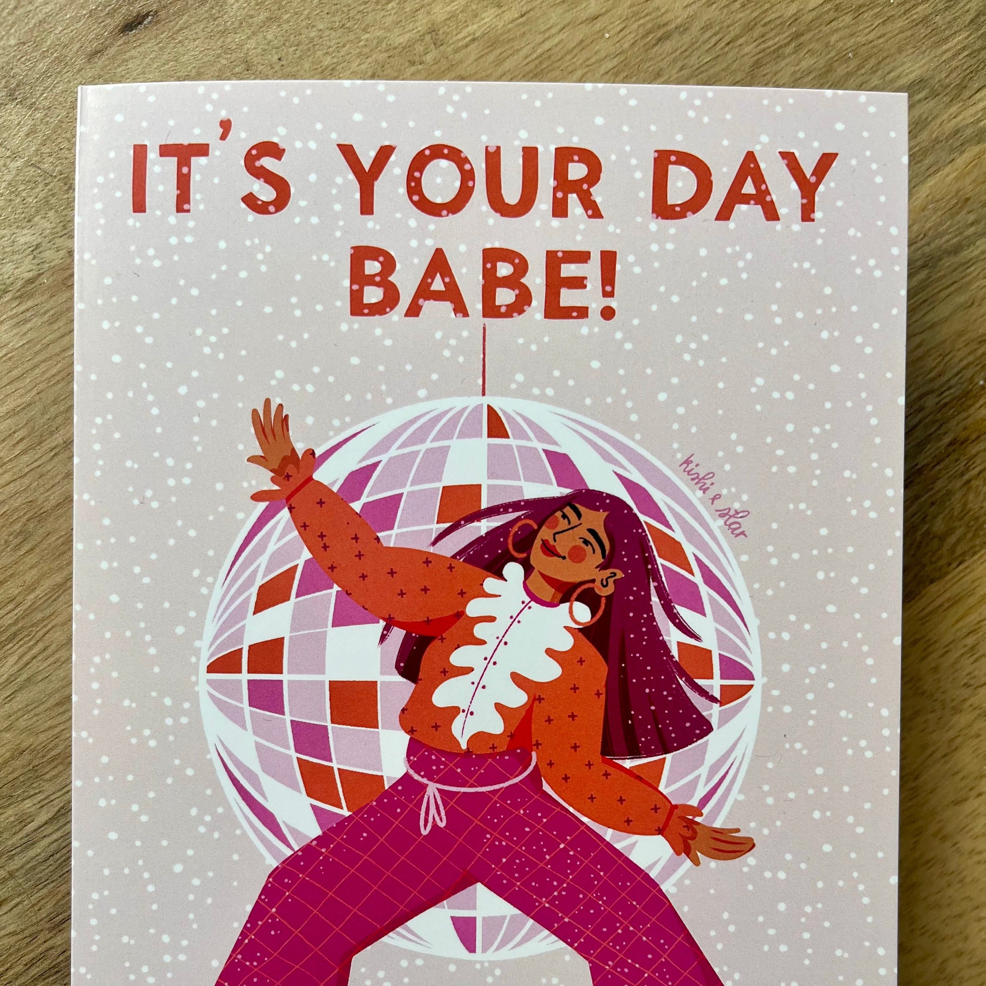 Card with illustration of a person in a polka dot dress and pink pants, surrounded by a disco ball, with 'It's Your Day Babe!' text above.