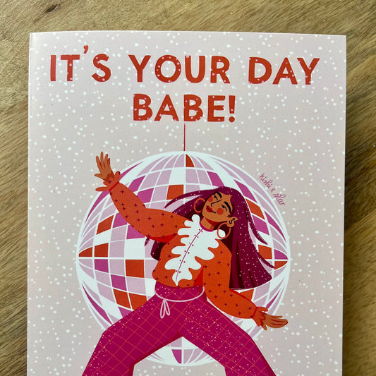 Card with illustration of a person in a polka dot dress and pink pants, surrounded by a disco ball, with 'It's Your Day Babe!' text above.