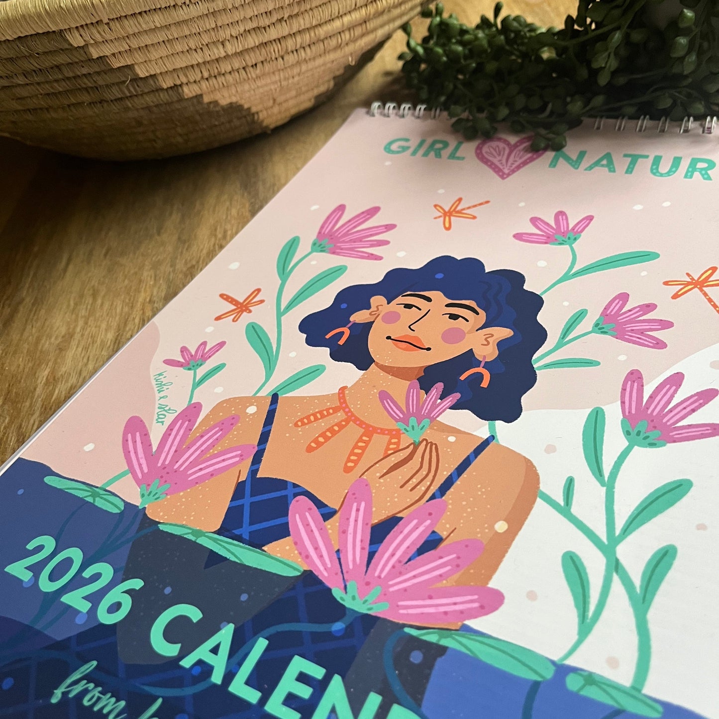 2026 calendar with a colorful design of a woman and flowers on a shelf.